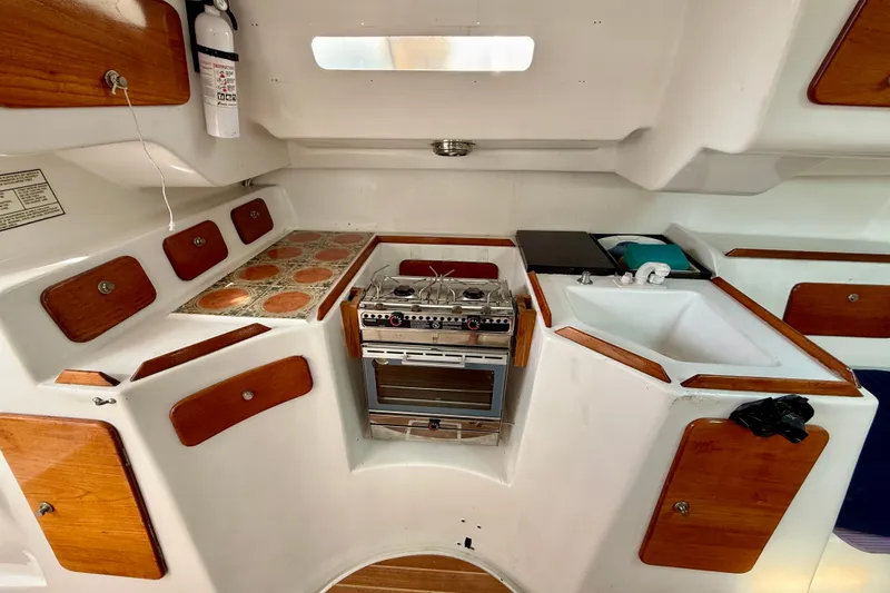 Slide: The Image of 1985 MacGregor 65 yacht kitchen with stove, sink, and wooden cabinets. - 23