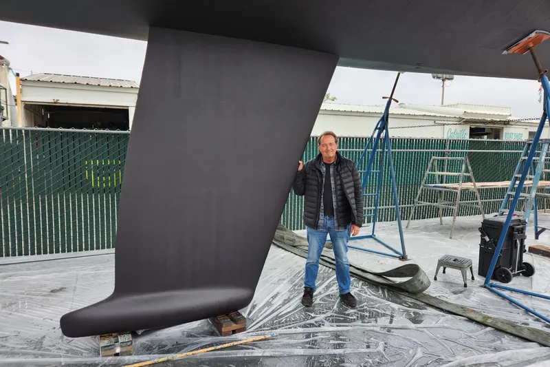 Slide: The Image of Man standing beside 1985 MacGregor 65 sailboat keel in a boatyard. - 37