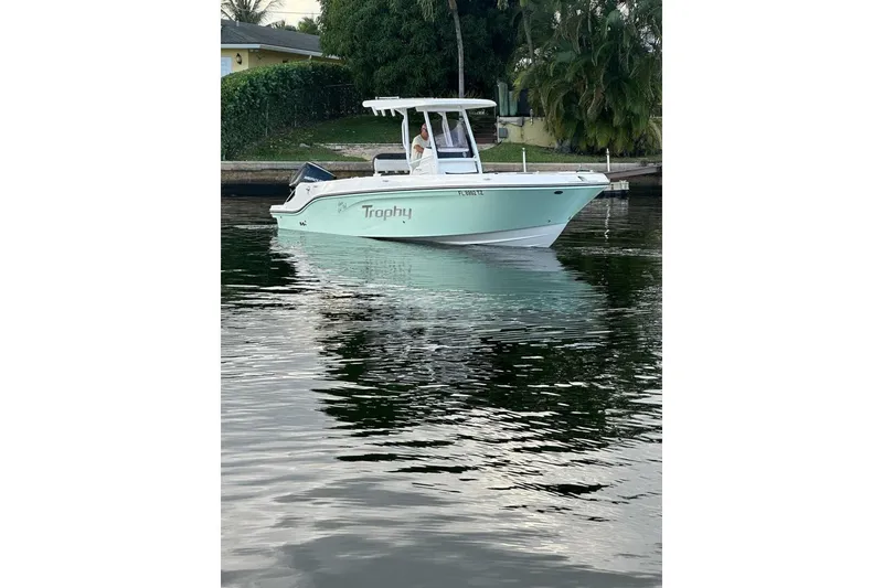 Slide: The Image of 2024 Bayliner Trophy T24CC boat on calm water, surrounded by lush greenery. - 19