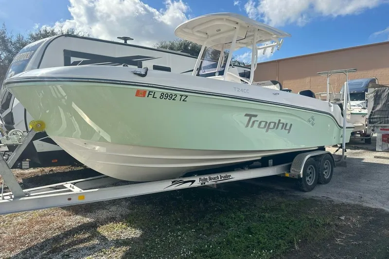 Slide: The Image of 2024 Bayliner Trophy T24CC boat on trailer, parked outdoors under a blue sky. - 25