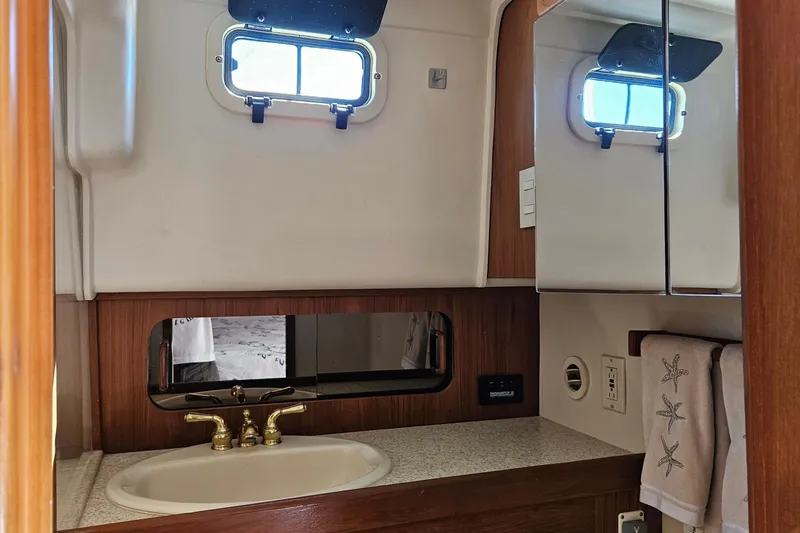 Slide: The Image of Bathroom interior of 1999 Mainship 430 Trawler with sink, mirror, and porthole window. - 13