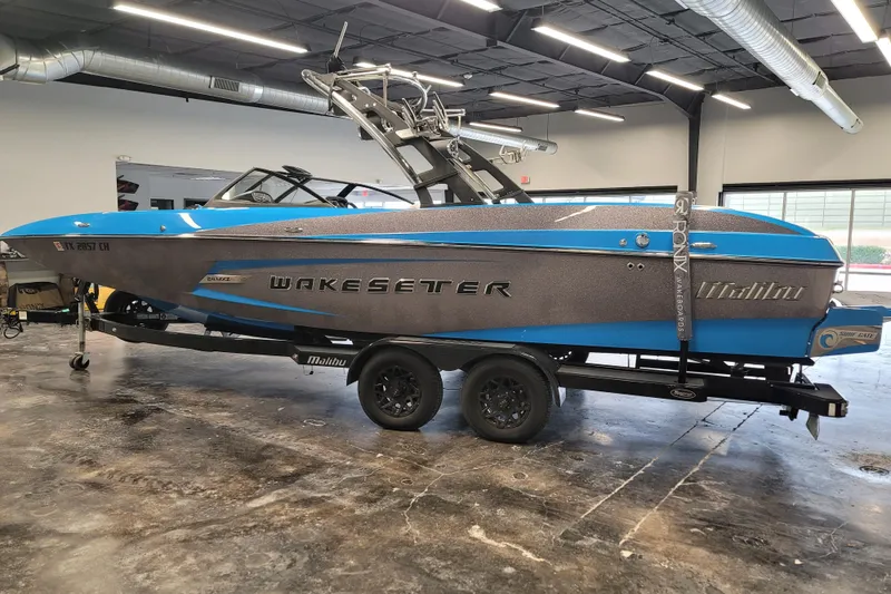 Slide: The Image of 2014 Malibu Wakesetter 24 MXZ boat in showroom, blue and gray design, on trailer. - 5