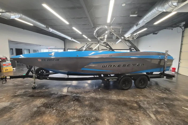Slide: The Image of 2014 Malibu Wakesetter 24 MXZ boat in a showroom, blue and gray exterior. - 9