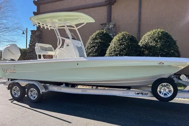 Slide: The Image of 2026 Mako 24 APEX boat on trailer, parked outdoors, side view. - 2