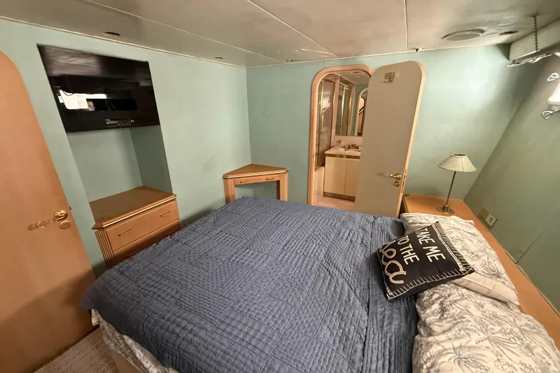Slide: The Image of 1990 Denison Pilothouse Motoryacht bedroom with blue bedding, TV, and ensuite bathroom. - 75