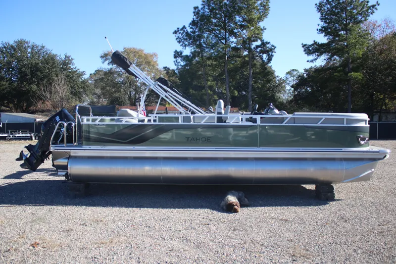 Slide: The Image of 2026 Tahoe Pontoon Sport 85 Rear Fish boat on gravel, surrounded by trees. - 2
