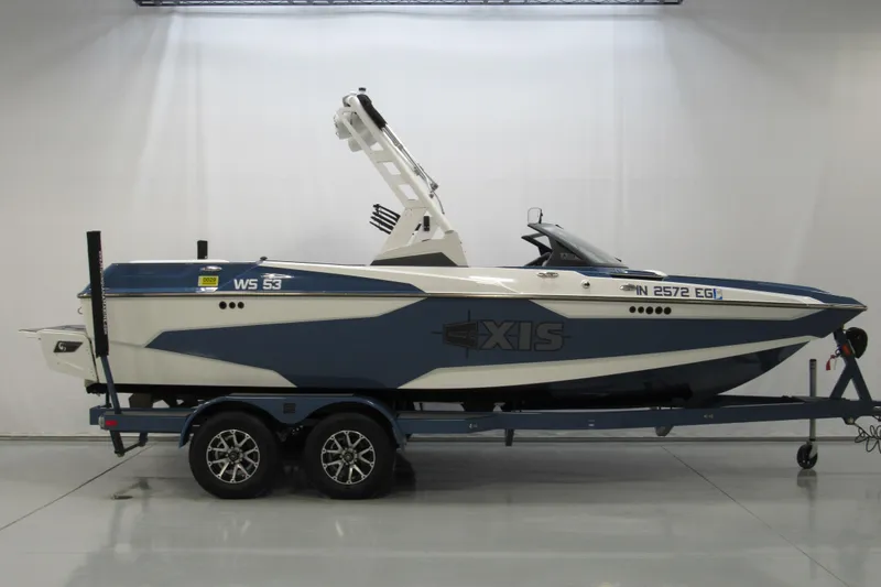 The Image of 2021 Axis A20 boat on trailer, blue and white design, displayed in a showroom. - 0
