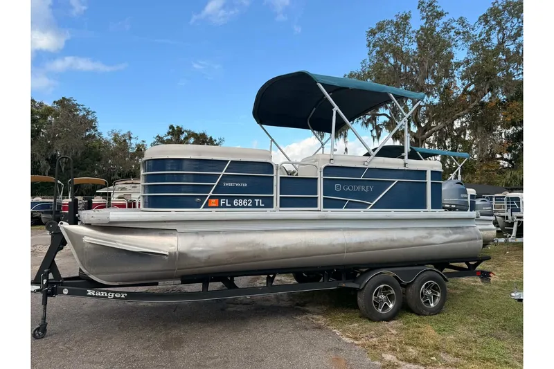 The Image of 2023 Sweetwater 2086 CX pontoon boat on trailer, blue canopy, parked outdoors. - 1