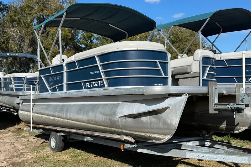 Slide: The Image of 2022 Sweetwater 2086 CX pontoon boat on trailer, blue and white design, parked outdoors. - 4