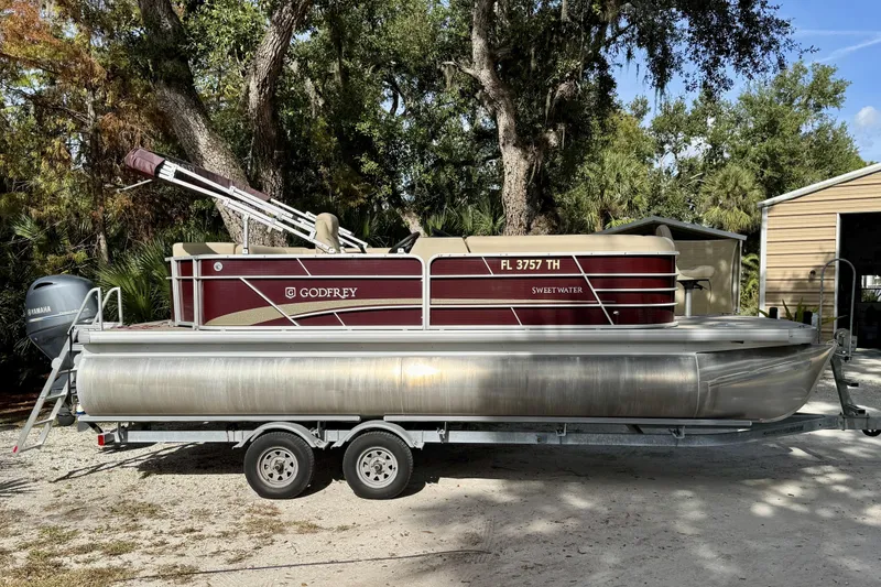 The Image of 2022 Godfrey Sweetwater 2286 C pontoon boat on trailer, surrounded by trees. - 0