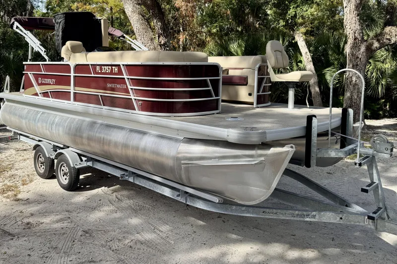 Slide: The Image of 2022 Godfrey Sweetwater 2286 C pontoon boat on trailer, parked in wooded area. - 2