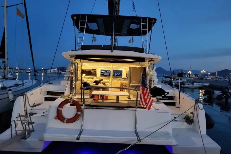 Slide: The Image of 2019 Bali 4.3 catamaran docked at marina during evening, illuminated interior, American flag displayed. - 2