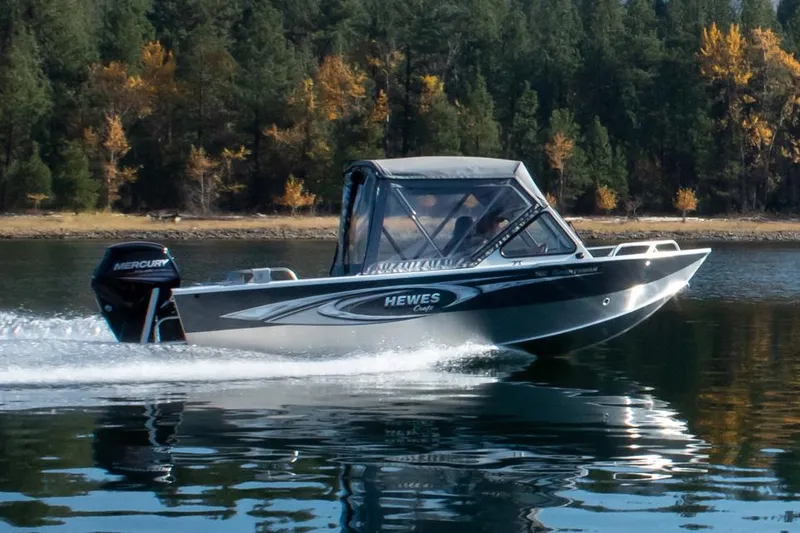 Slide: The Image of Manufacturer Provided Image: 2026 Hewescraft 180 Sportsman boat cruising on a lake with forested shoreline. - 4