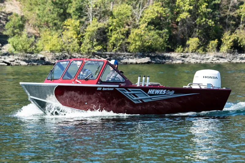 Slide: The Image of Manufacturer Provided Image: 2026 Hewescraft 180 Sportsman boat cruising on a lake with lush green shoreline. - 6