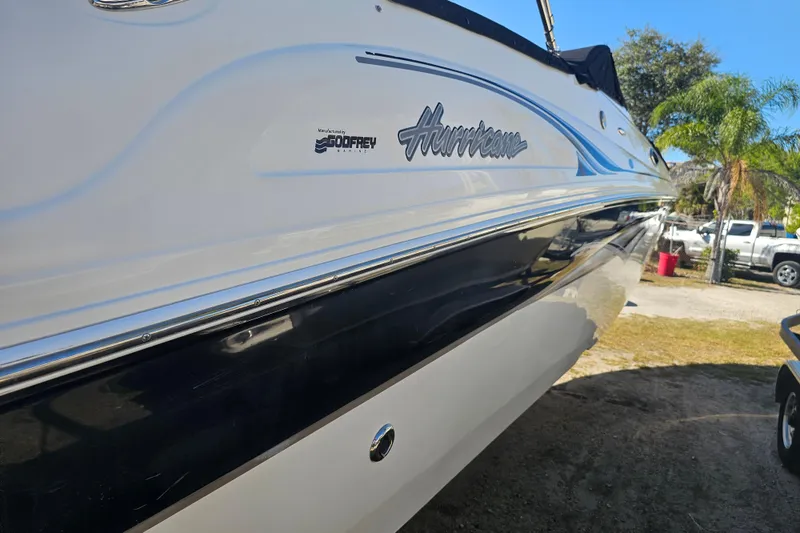 Slide: The Image of 2006 Hurricane SunDeck 260 OB boat, side view with logo, parked outdoors. - 4