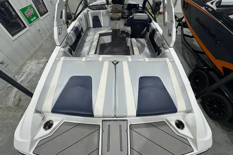 Slide: The Image of 2019 Malibu Wakesetter 21 MLX interior with gray and blue seating, docked indoors. - 7