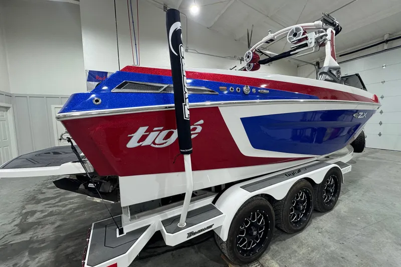 Slide: The Image of 2021 Tigé 25ZX boat in showroom, red and blue design on trailer. - 18