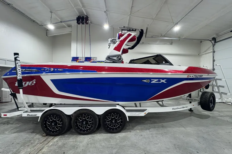 Slide: The Image of 2021 Tigé 25ZX boat in showroom, red and blue design on trailer. - 19