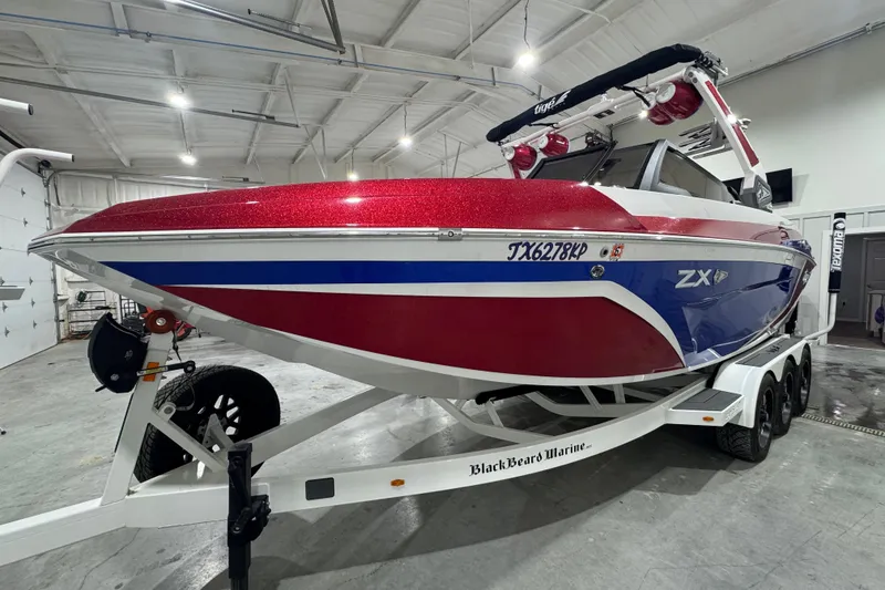 Slide: The Image of 2021 Tigé 25ZX boat with red and blue design on a trailer in showroom. - 21