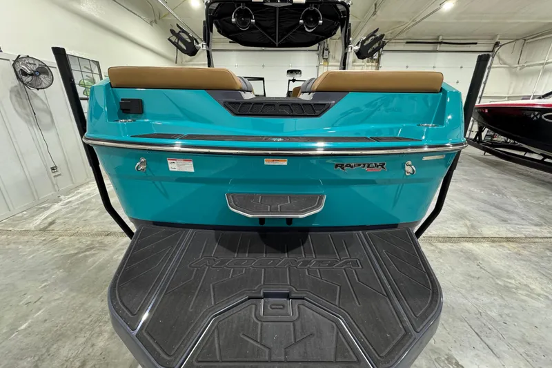 Slide: The Image of 2026 Moomba Tykon boat rear view in a showroom, featuring teal color and Raptor engine branding. - 3