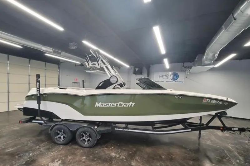 The Image of 2022 MasterCraft NXT24 boat in showroom, green and white design on trailer. - 1