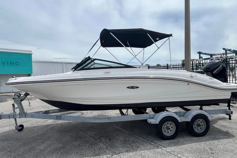The Image of 2023 Searay 210SPX boat on trailer with black canopy, parked outdoors. - 1
