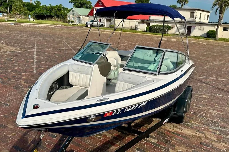 Slide: The Image of 2012 Regal 2100 Bowrider boat with blue canopy on a trailer, parked on brick pavement. - 9