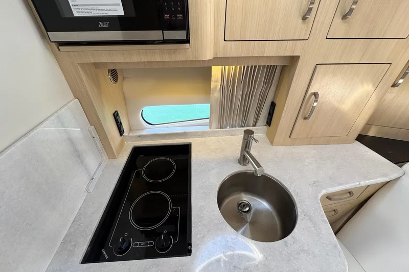 Slide: The Image of 2026 Regal 33 XO yacht kitchen with stove, sink, and wooden cabinetry. - 79