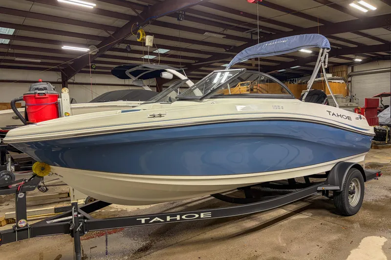 The Image of 2023 Tahoe 185 S boat in a warehouse, blue and white design on trailer. - 1