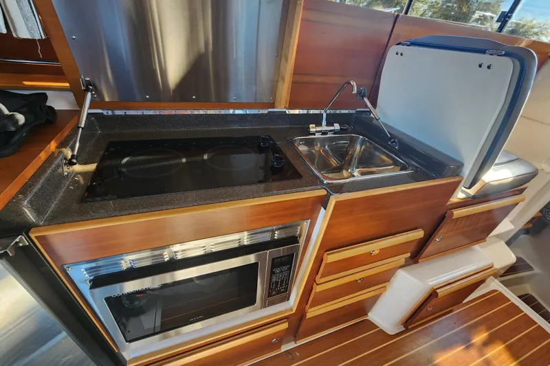 Slide: The Image of 2021 Cutwater C-32 CB galley with stove, sink, and microwave in a compact wooden design. - 34