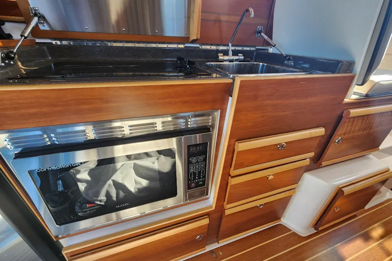 Slide: The Image of 2021 Cutwater C-32 CB galley with microwave, sink, and wooden cabinetry. - 76