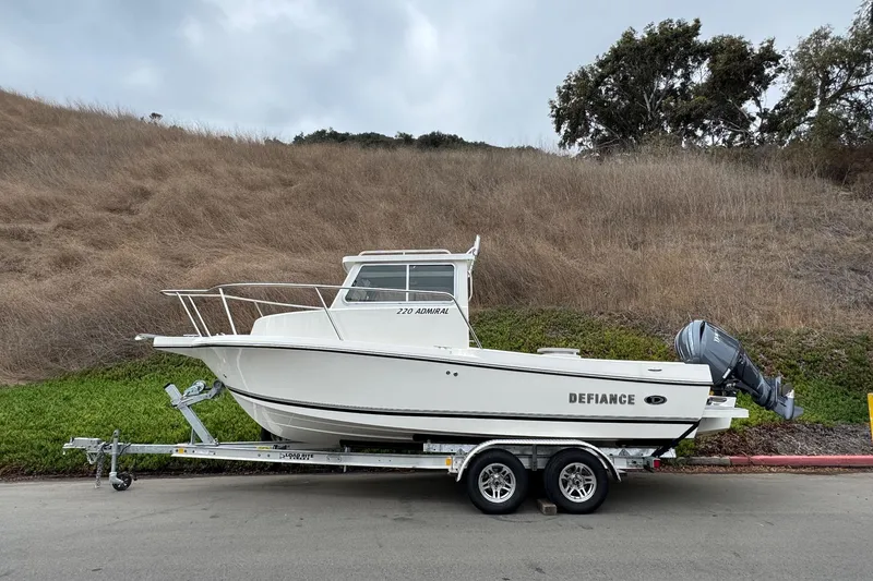 Slide: The Image of 2026 Defiance Admiral 220 EX boat on trailer, parked roadside with grassy hill background. - 2