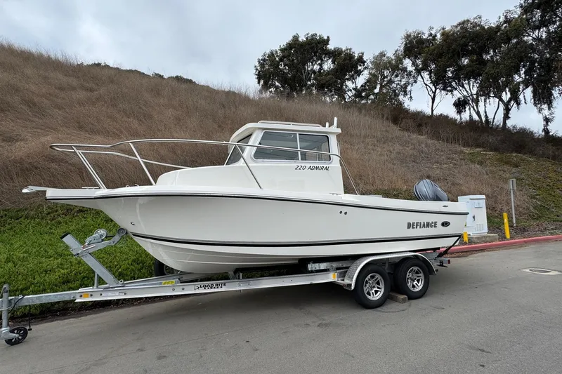 Slide: The Image of 2026 Defiance Admiral 220 EX boat on trailer, parked roadside with grassy hill background. - 5