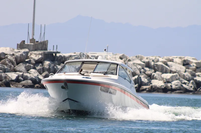 Slide: The Image of 2019 Pursuit DC 365 Dual Console boat navigating near rocky shoreline. - 2