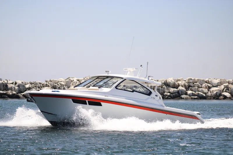 Slide: The Image of 2019 Pursuit DC 365 Dual Console boat cruising on water near rocky shoreline. - 4