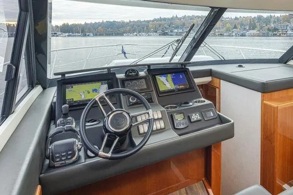 Slide: The Image of 2019 Riviera 395 SUV helm with navigation screens and steering wheel, overlooking a scenic waterway. - 12