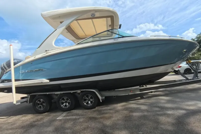 Slide: The Image of 2018 Regal 29 OBX boat on trailer, blue hull, parked outdoors under blue sky. - 29