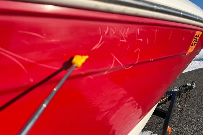 Slide: The Image of 2010 Chaparral 216 SSi boat with red hull, showing scratches and repair work. - 12