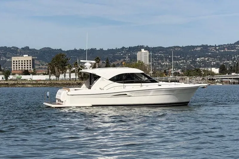 The Image of 2007 Riviera 3600 Sport Yacht cruising on a calm waterway with scenic city backdrop. - 0