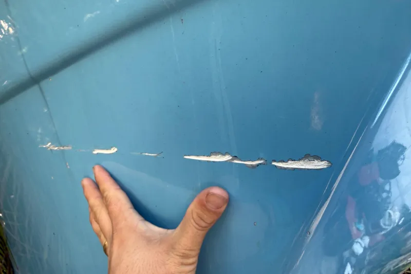 Slide: The Image of Hand inspecting scratches on blue 2002 Fishmaster 212 Travis Edition boat hull. - 36