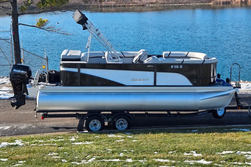 The Image of 2023 Crest Classic LX 200 pontoon boat on trailer by a lake. - 0
