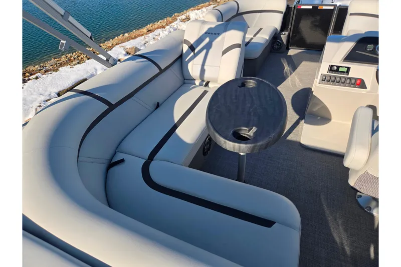 Slide: The Image of 2023 Crest Classic LX 200 pontoon boat interior with seating and table by the water. - 19
