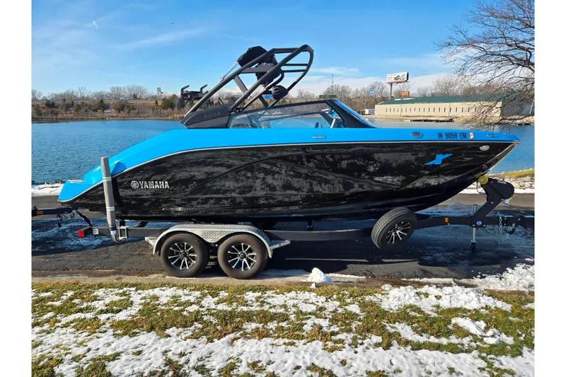Slide: The Image of 2023 Yamaha Boats 222XD in blue and black on trailer by a lake. - 9