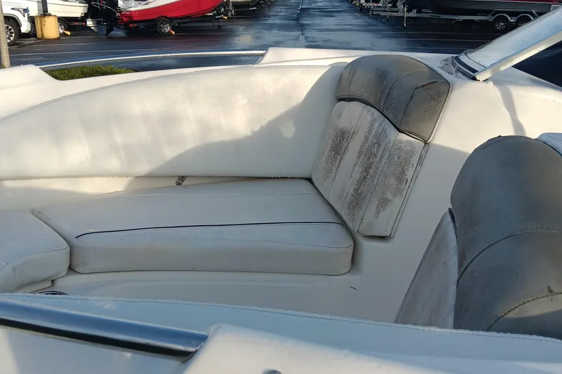 Slide: The Image of 2013 Bayliner 215 Bowrider interior with white and gray seating, parked in a marina. - 14