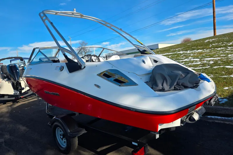 Slide: The Image of 2011 Sea-Doo 180 Challenger SE boat with red hull on trailer, parked outdoors. - 3