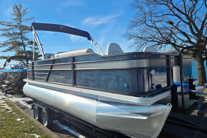Slide: The Image of 2022 Crest Classic Fish 200 pontoon boat on trailer, parked near trees and water. - 8