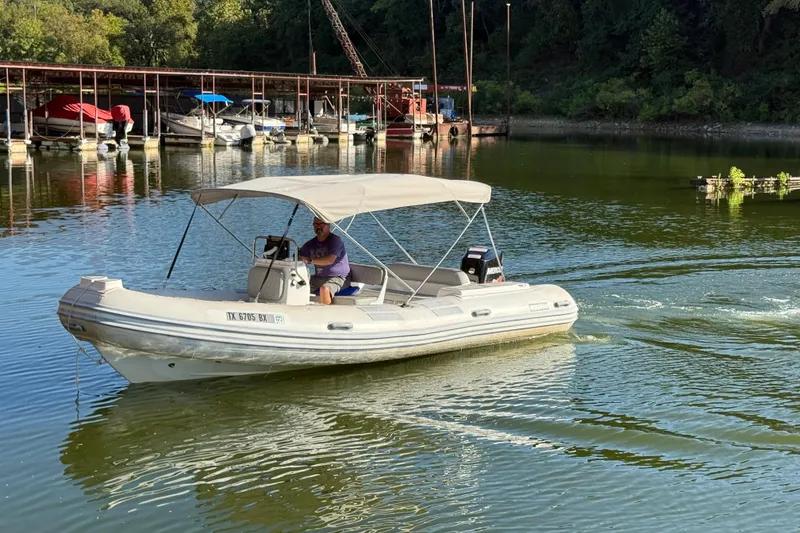 Slide: The Image of 2005 Caribe DL20 boat cruising on a calm lake near a marina. - 6