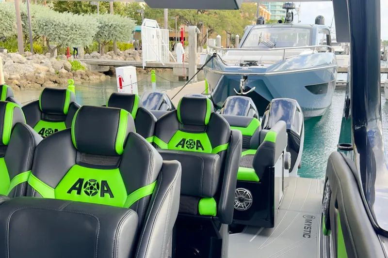 Slide: The Image of 2026 Mystic Powerboats M5200 XL Cabin with green and black seating at a marina. - 18