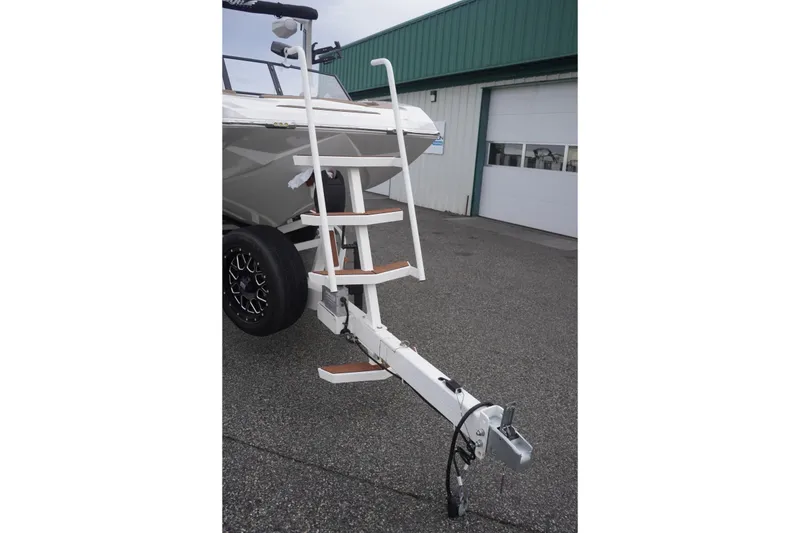 Slide: The Image of 2023 Tigé 24RZX boat trailer with steps, parked outside a green building. - 20