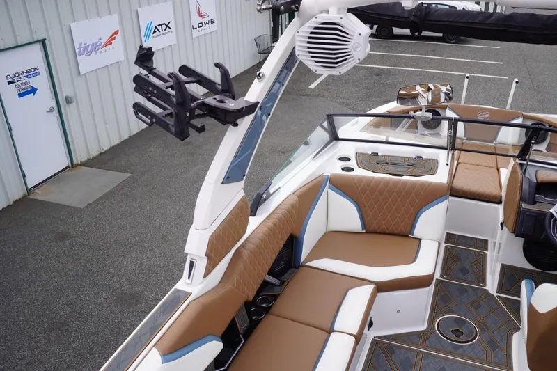 Slide: The Image of 2023 Tigé 24RZX boat interior with brown and white seating, docked near showroom. - 36